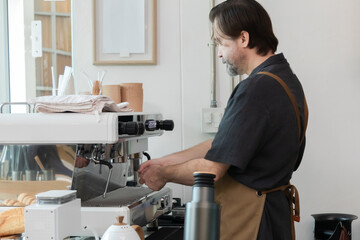 Senior barista in an apron operates a coffee machine at his small business. man focus and experience reflect a lifestyle of independence, craftsmanship, and pride in daily work entrepreneurship