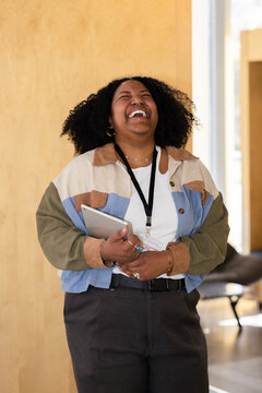 Black woman joyfully laughing while embracing a digital tablet