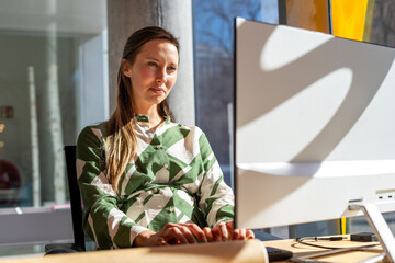 Woman in green shirt working on computer in sunlight