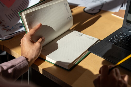 Hands flipping pages of a planner near a laptop and pencil