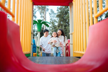 Happy family playing on a colorful slide in a playground
