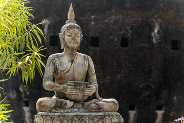 Obraz premium Stone Buddha statue in meditation pose holding alms bowl. Copy space spiritual calm background
