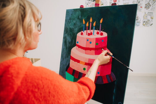 Artist painting colorful layered birthday cake on canvas
