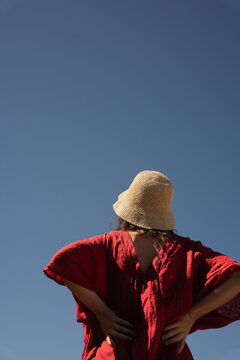 Woman in straw hat and red dress against blue sky.
