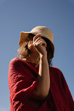 Woman in straw hat and red dress against blue sky.