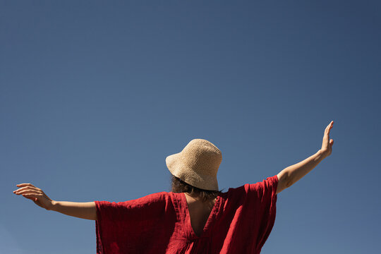 Woman in straw hat and red dress against blue sky.