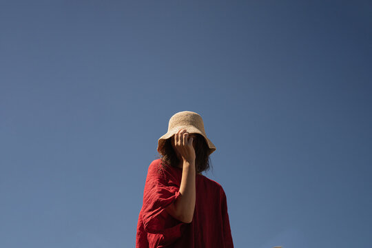 Woman in straw hat and red dress against blue sky.