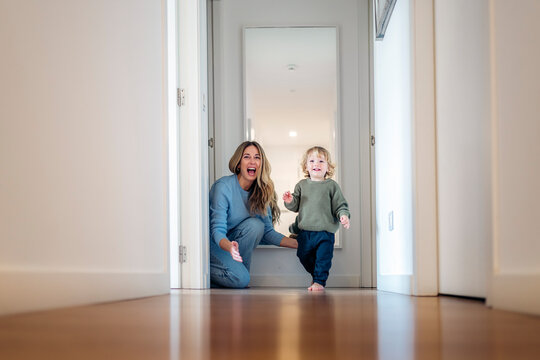 Mother encouraging toddler taking first steps in corridor at home