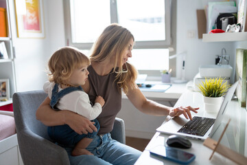 Busy mother working from home, holding her baby and talking on laptop