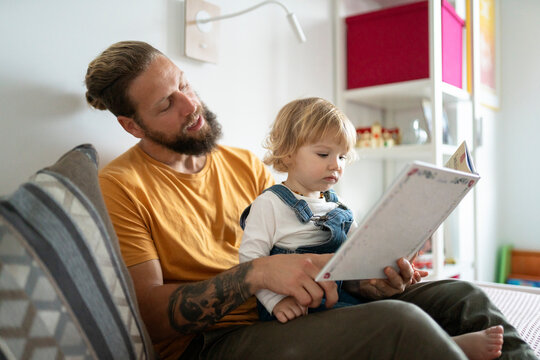 Father reading book with toddler daughter at home