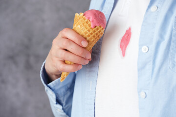 Close-up of pink ice cream in a cone falling onto white clothes during a sweet moment. Concept of...