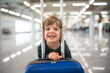 Happy child smiling behind suitcase at airport terminal