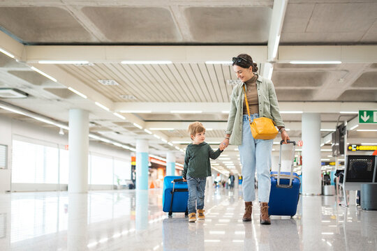 Mother and son walking through airport terminal pulling suitcases