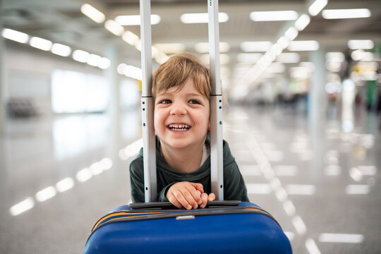 Happy child smiling behind suitcase at airport terminal