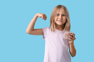 Fototapeta premium Cute little girl with glass of sweet chocolate milk showing muscles on blue background
