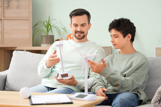 Teenage boy and his father with wind turbine models talking on sofa at home