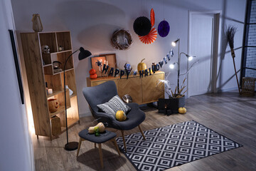 Interior of festive living room with armchair, commode and Halloween decorations in evening