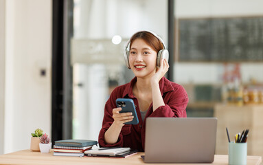 Young asian happy Hispanic Asian student wearing headphones talking on online call using laptop in university campus office. College female student learning remotely.
