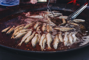 cooking fish in large round frying pan outdoors, fried smelt, close-up view, street food concept