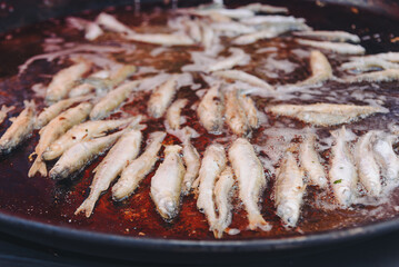 cooking fish in large round frying pan outdoors, fried smelt, close-up view, street food concept