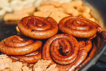 fried sausages frying in large pan outdoors, street food concept