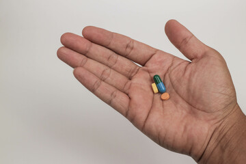 Close-up hand holding a variety of colorful pills and capsules, including round tablets on a plain background.