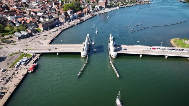 Aerial footage of the open bascule bridge with sailboats passing through, surrounded by old town buildings, harbor and waterfront caf&eacute;s, Kappeln, Schleswig-Holstein, Germany. Town of Kappeln on Schlei