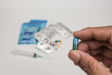 Close-up of a hand holding a single tablet with blurred medical supplies in the background