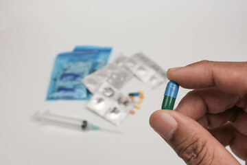 Close-up of a hand holding a single tablet with blurred medical supplies in the background