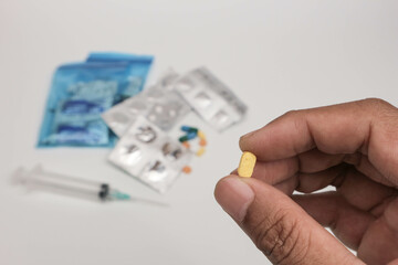 Close-up of a hand holding a single tablet with blurred medical supplies in the background