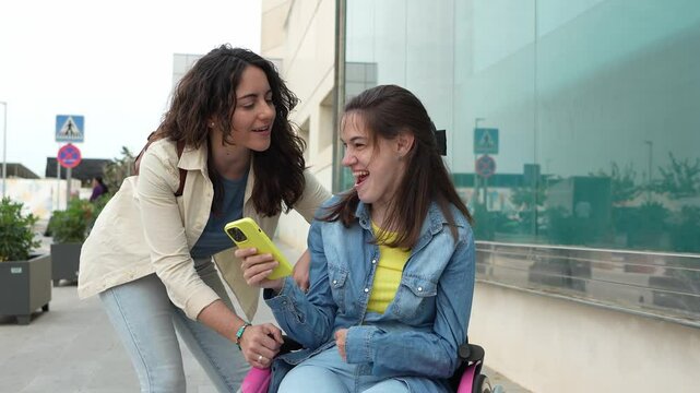 Young woman with cerebral palsy showing phone content to caregiver outdoors - Sharing moments, inclusion, disability awareness. Cerebral palsy concept.