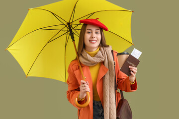 Female tourist in autumn clothes with passport and umbrella on green background