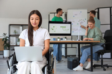 Young Asian woman in wheelchair working with laptop at office. Green energy concept
