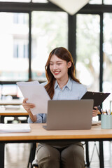 Smiling Young asian accountant business woman working with documents using calculator and laptop...