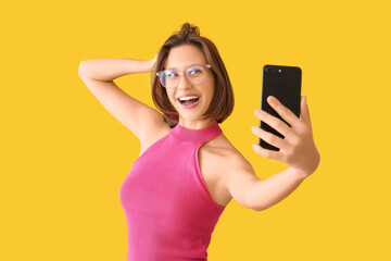 Naklejka premium Pretty young woman with mobile phone taking selfie on yellow background
