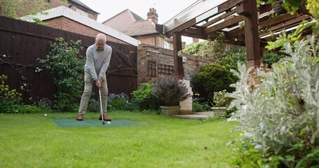 Golf, ball and senior man in garden for sports, training and relax with hobby on artificial grass. Game, putting course challenge and club on green lawn with stroke, hit and swing in backyard of home - Powered by Adobe