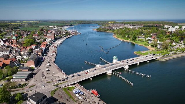 Aerial footage of Kappeln on Schlei fjord  with historic old town, harbor and bridge with flowing traffic, all surrounded by spring landscape of Schleswig-Holstein, Germany.
