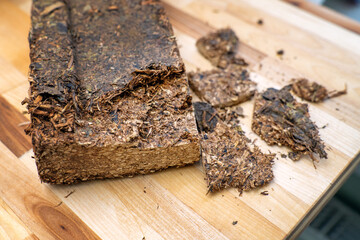 dense lactation tea brick chopped into pieces on a wooden board, prepared for brewing to support...