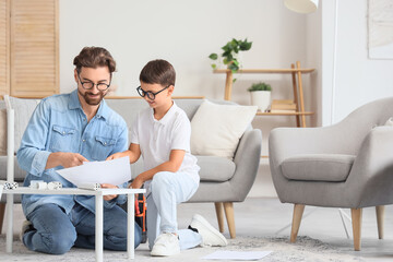 Father with instructions and his little son assembling shelf unit at home