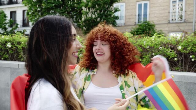 Young women celebrating diversity, holding colorful rainbow flags, expressing unity and empowerment with jubilant gestures in sunny urban park setting