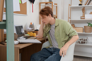 Stressed male student studying at table in room