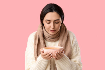 Sick young woman with tasty soup on pink background