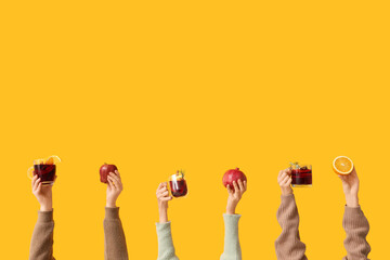Female hands with fruits and mugs of tasty mulled wine on yellow background
