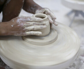 Young artisan shaping clay pot on spinning wheel in ceramic workshop
