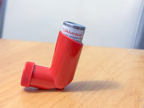 Calgary, Alberta, Canada. May 1, 2025. A red Alvesco inhaler on a wooden surface against a blurred background. The medication canister partially visible at the top.