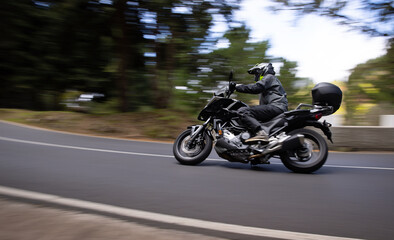 Driver riding motorcycle on empty asphalt road, blurred motiion, spring mountains