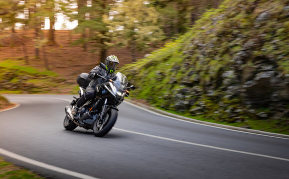 Driver riding motorcycle on empty asphalt road, blurred motiion, spring mountains - Powered by Adobe