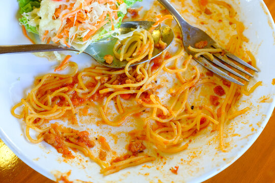 Finished Plate of Spaghetti,This close-up shot shows the remnants of a spaghetti meal served on a white plate. Strands of spaghetti coated in a red sauce are scattered across the plate, indicating the