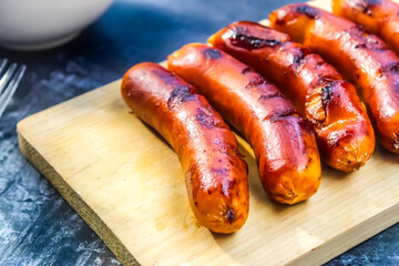 close up of grilled sausages on a cutting board with sauce on a black background