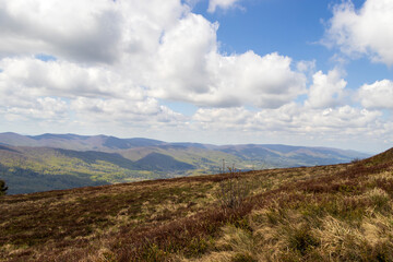 Scenic landscape view of Bieszczady mountains with lush greenery under a bright blue sky dotted with fluffy clouds. Perfect for nature enthusiasts and outdoor promotions.